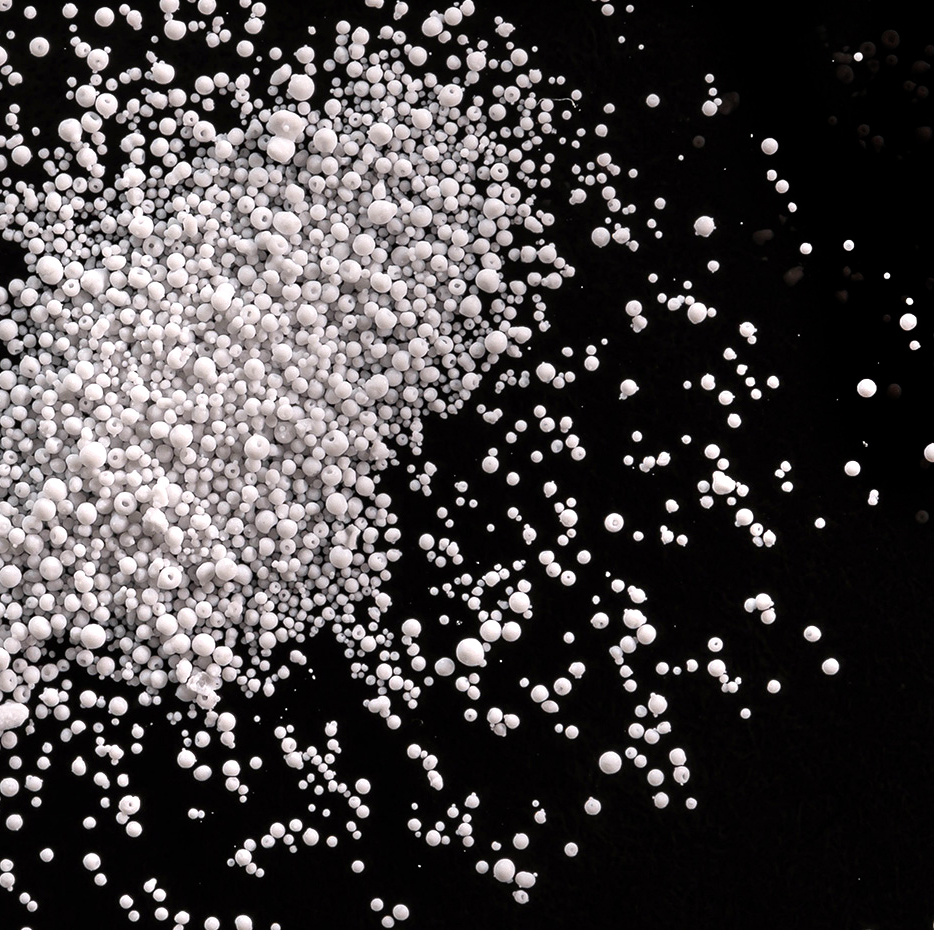 Overhead view of small white bead shaped media scattered across a black surface.
