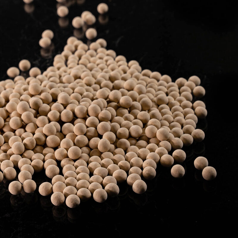Tan spherical beads in a pile on a black background.